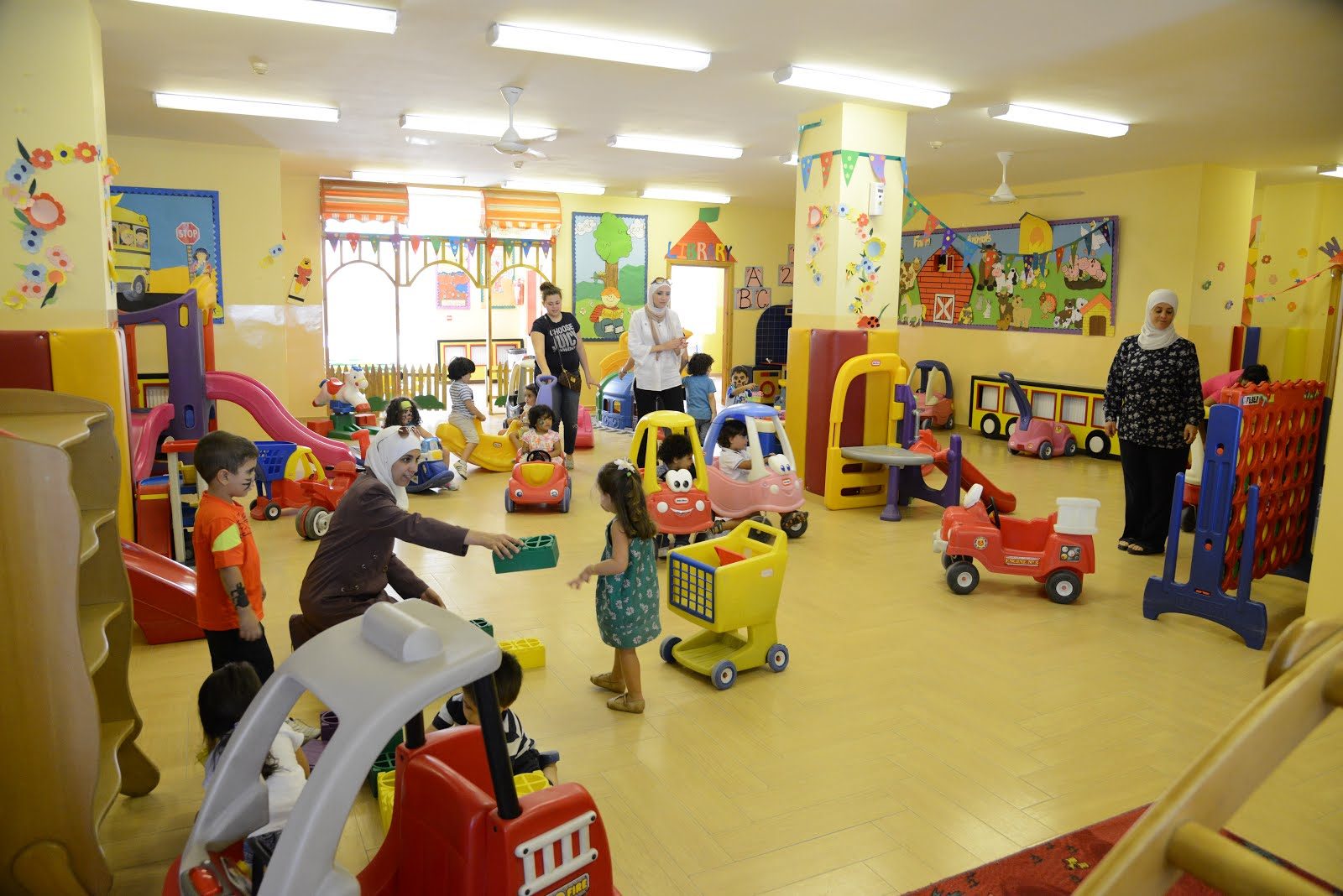 The large indoor play area full of ride-on toys and teachers